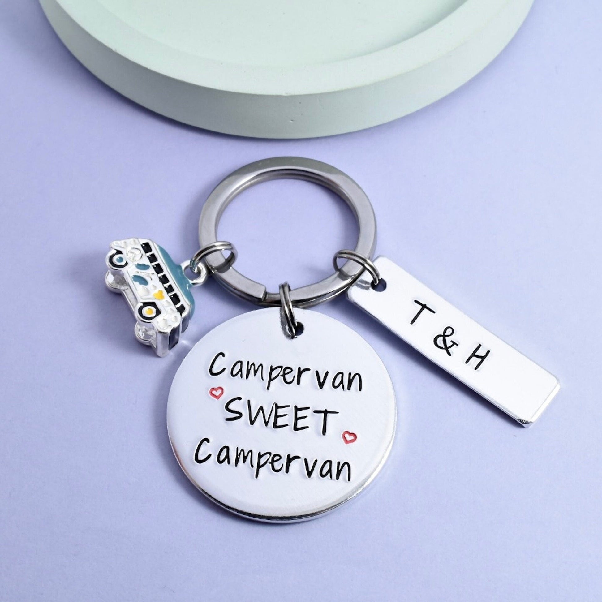 A keyring with a round aluminium disc stamped with 'Campervan Sweet Campervan' and an aluminium rectangle tag with the initials 'T & H'. Also includes a small campervan charm and a split ring.