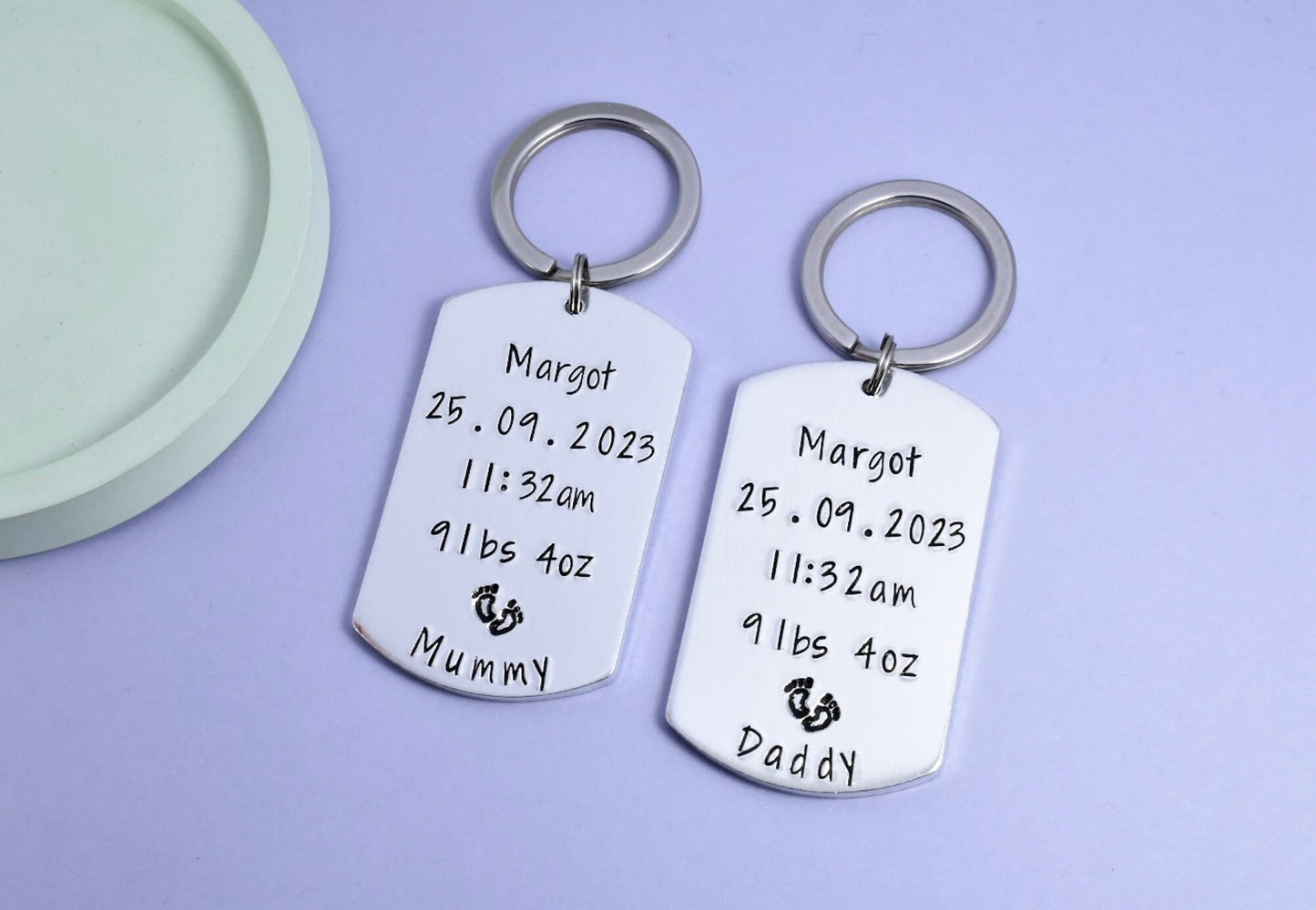 Two personalised birth keepsake keyrings with 'Mummy' and 'Daddy' stamped on them, along with birth details and footrint design. New Mummy and Daddy keyring set
