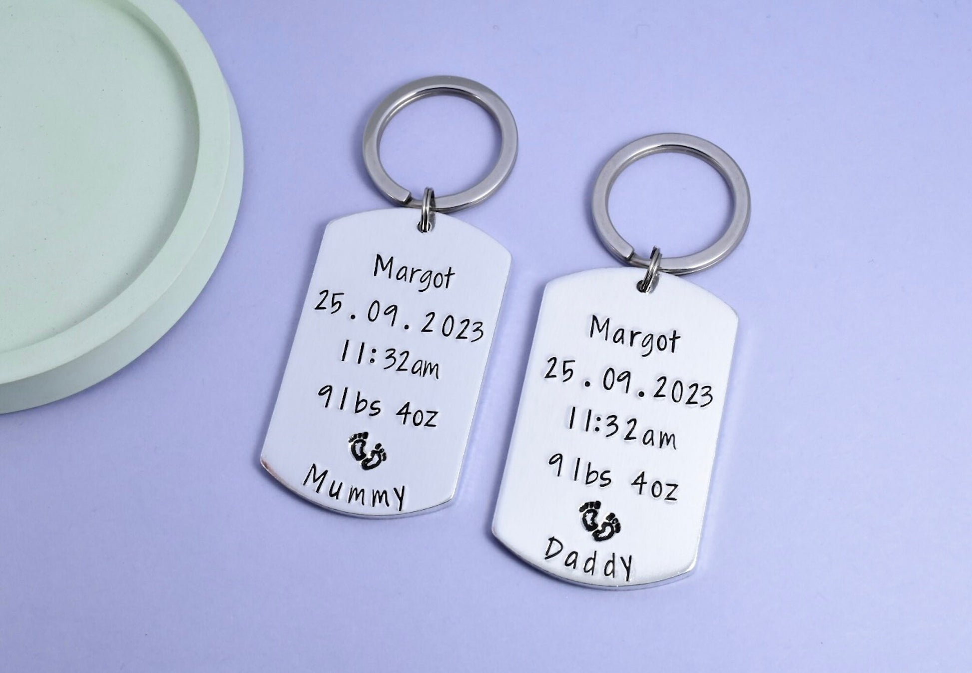 Two personalised birth keepsake keyrings with 'Mummy' and 'Daddy' stamped on them, along with birth details and footrint design. New Mummy and Daddy keyring set