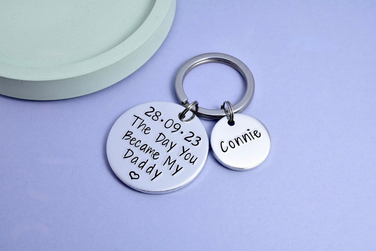 A keyring with two aluminium discs, one large with a birthdate and the words 'The Day You Became My Dada', and one small with the name 'Connie'.