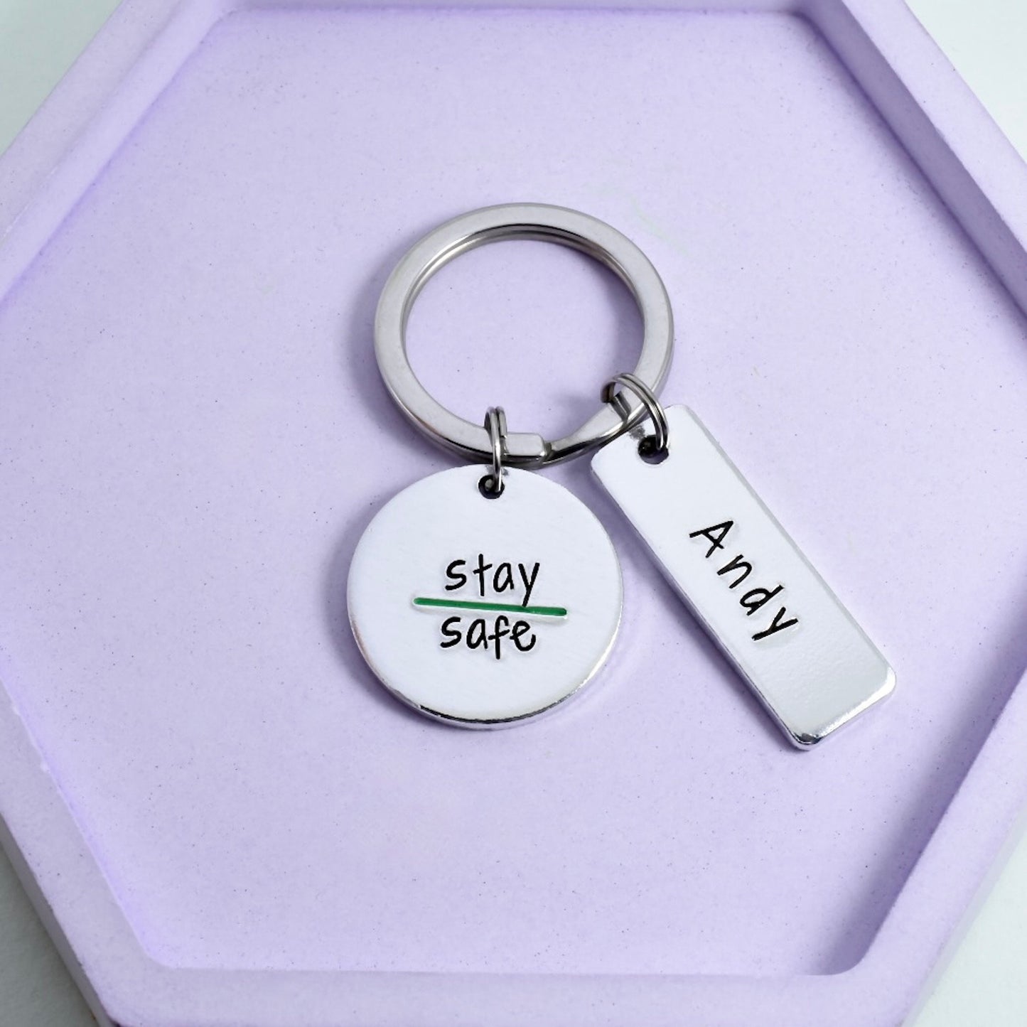 A silver paramedic keyring with two aluminium tags, one circular with the phrase 'stay safe' stamped on it, and one rectangular tag with the name 'Andy' stamped on it. thin green line kerying