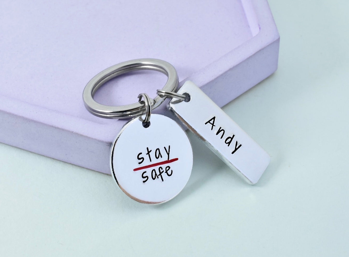 A personalised fire person keyring with a thin red line design, the larger disc is aluminium with 'stay safe' written on it, and the rectangle is also aluminium with the name 'Andy'.