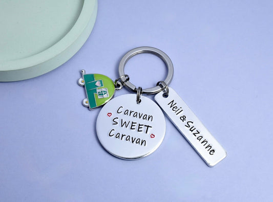 A keyring with a round aluminium disc stamped with 'Caravan Sweet Caravan' and a rectangular tag with personalised text. There's also a small caravan charm in green or pink attached to the keyring.